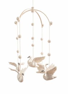 three white birds are flying in the air with balls hanging from it's sides