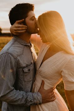 a man and woman kissing each other in an open field at sunset with the sun behind them