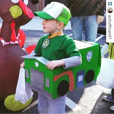 a young boy in a green costume standing next to a cardboard box shaped like a train