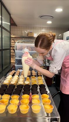 a woman is pouring frosting on cupcakes