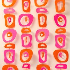 an assortment of pink and orange shapes hanging from strings on a wall in front of a white background