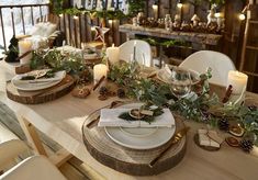 the table is set for christmas dinner with candles and greenery on it, along with other festive items