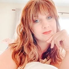 a woman with long red hair and blue eyes is posing for the camera while sitting on a bed