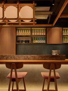 two wooden stools sit in front of a bar with bottles on the back wall