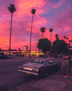 an old car parked on the side of the road in front of some palm trees