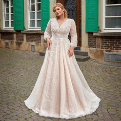 a woman standing in front of green shutters wearing a wedding dress with long sleeves