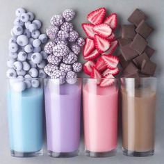 three glasses filled with different types of candy and strawberries next to milkshakes