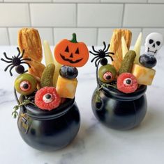 two black pots filled with halloween food on top of a table