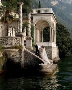 a bride and groom are standing on some steps by the water with mountains in the background