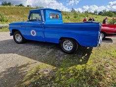 an old blue pickup truck parked on the side of a road with people in it