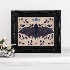 a black frame with a bat on it next to some flowers and a vase filled with white flowers