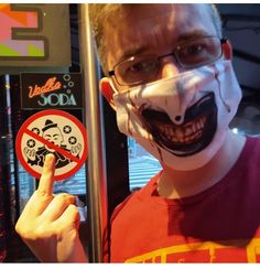 a man wearing a face mask and holding up a sign with an evil clown on it