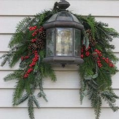 a lantern hanging from the side of a house decorated with greenery and red berries