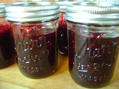 four jars filled with red liquid sitting on top of a wooden table next to each other