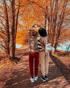 two young women walking down a path in the fall with trees and water behind them