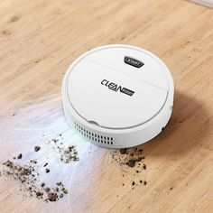 a white robot vacuum sitting on top of a wooden floor next to dirt and clumps