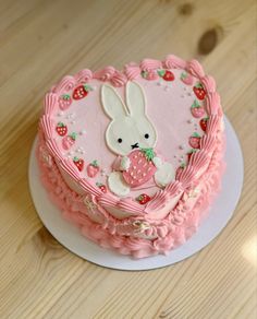 a pink cake decorated with a bunny holding a strawberry in the shape of a heart