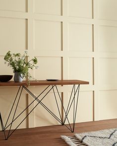 a table with some flowers on it and a rug in front of the wall behind it