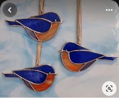 three stained glass birds are hanging on a wall ornament in blue, orange and white