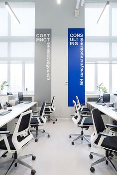 an office with white desks and black chairs in front of large windows that have blue signs on them