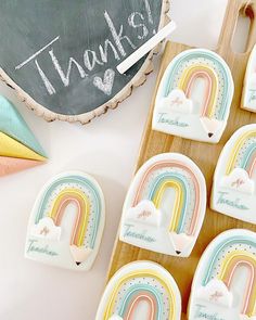 cookies decorated with rainbows and clouds are on a tray next to a chalkboard