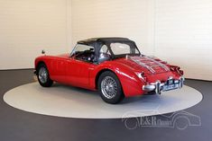 an old fashioned red sports car parked in a garage with its hood up and the top down