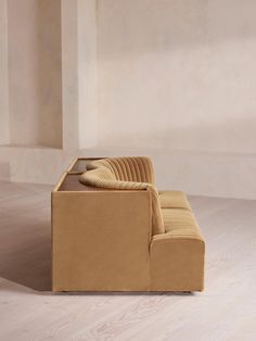 a tan couch sitting on top of a hard wood floor next to a white wall