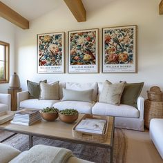 a living room filled with white furniture and paintings on the wall above it's coffee table