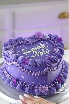 a heart shaped cake with purple frosting and flowers on it, sitting on a table