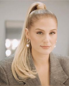 a woman with long blonde hair wearing earrings and a gray jacket is looking at the camera