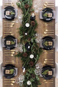 the table is set with black plates and silverware, pine cone centerpieces