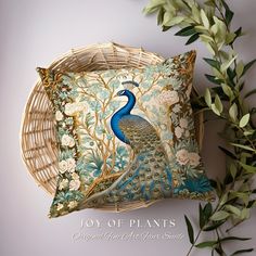 a decorative peacock pillow sitting on top of a wicker basket next to a plant