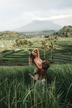 two people in the middle of some tall grass with mountains in the backgroud