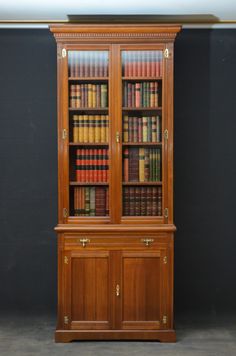 an old wooden bookcase with many books on the top and bottom shelves, in front of a black wall