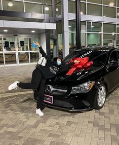 a person sitting on the hood of a car in front of a building wearing a face mask