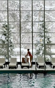 a woman sitting on the edge of a swimming pool next to a large glass window