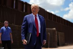 a man in a blue suit and red tie standing next to a fence with two men walking behind him