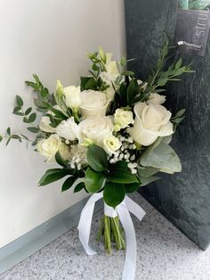 a bouquet of white roses and greenery in front of a wall with a sign