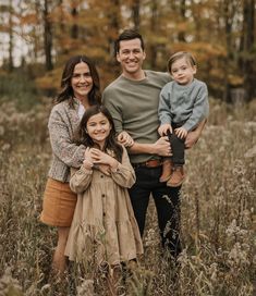 a family poses for a photo in the middle of a field with tall grass and trees