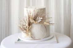 a white wedding cake with dried flowers and leaves on top, sitting on a table