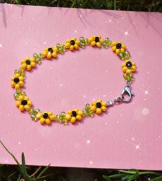 a yellow and black beaded bracelet with silver clasp on pink surface surrounded by grass