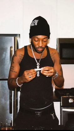 a man in a black tank top is looking at his cell phone while standing in the kitchen