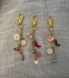 four key chains with charms attached to them on a gray fabric background, one has a flower and the other is a bird