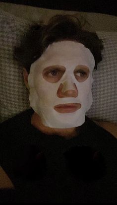 a man laying down with a white mask on his face and one eye open in front of him