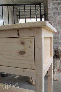 a dog is standing next to a wooden table with drawers on the top and bottom