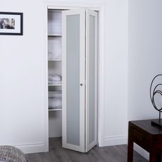 a bedroom with white walls and wooden flooring has an armoire in the corner