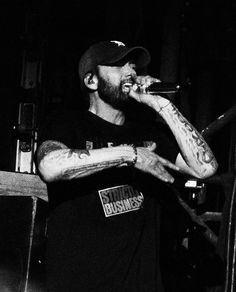 black and white photograph of a man with tattoos on his arm singing into a microphone