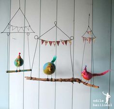 three colorful birds are perched on branches and hanging from the ceiling, with strings attached to them