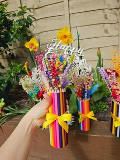 someone holding up some colorful pencils with flowers in them