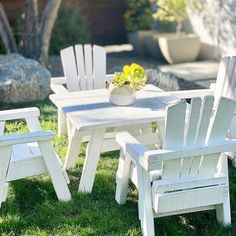 a white table and chairs sitting on top of a grass covered field next to a potted plant